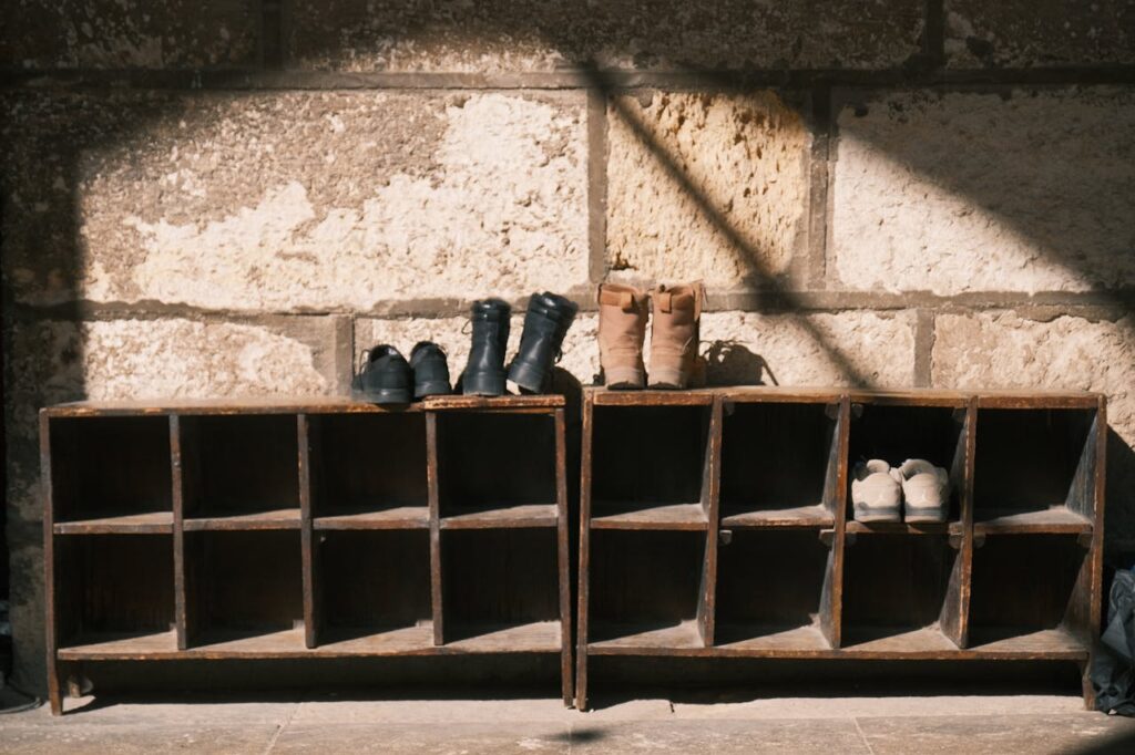 Weathered shoe rack holding various shoes against a stone wall, with natural lighting.
